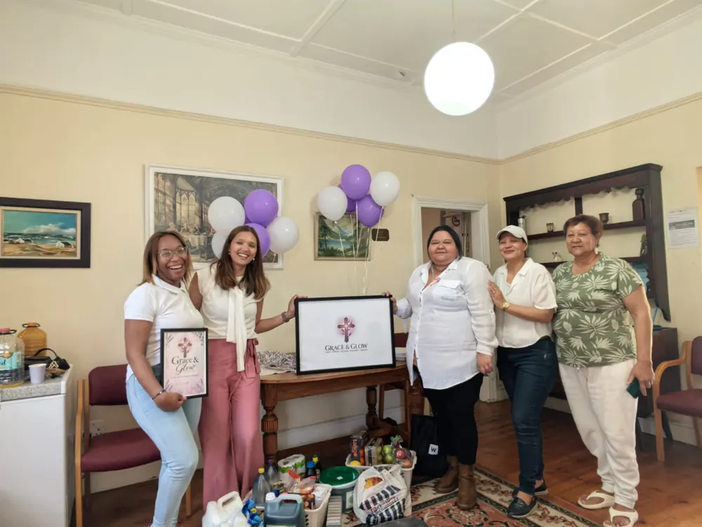 Women of Grace & Glow holding the framed logo beside balloons and donated supplies